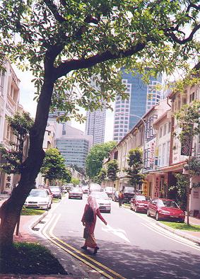 Mulher indiana cruza rua de casas tombadas, em meio ao centro financeiro de Singapore